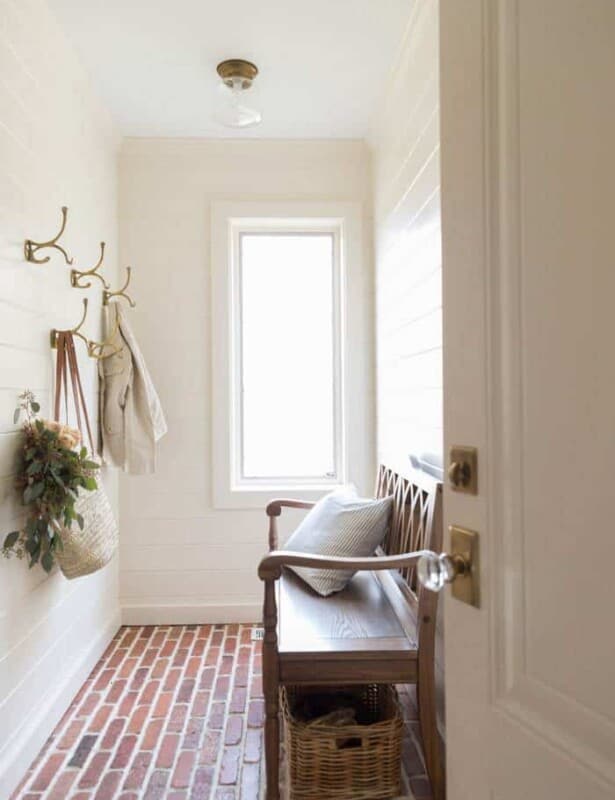 白色搭叠寄存室与薄砖地板,墙上黄铜钩和一个板凳。